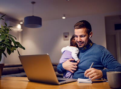 papa thuis aan het werk met een baby op de arm